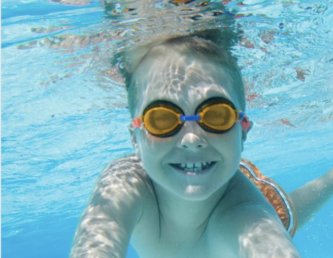 Jongen onder water met zwembril op kijkt in camera