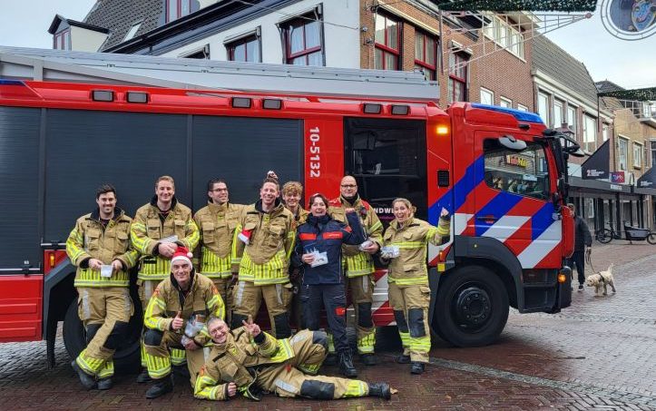 Kerstactie brandweer fijne veilige feestdagen met de brandweer poserend voor een brandweerauto in kerstsferen.