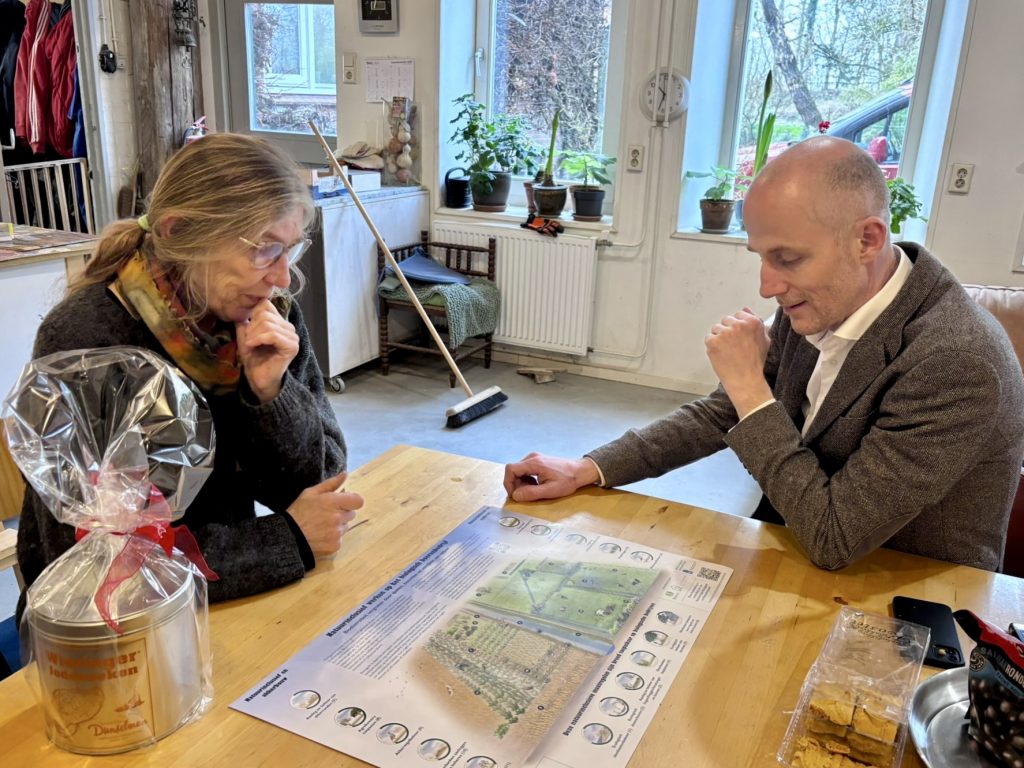 Silvia en Robert aan de keukentafel. Er ligt een plattegrond op tafel.