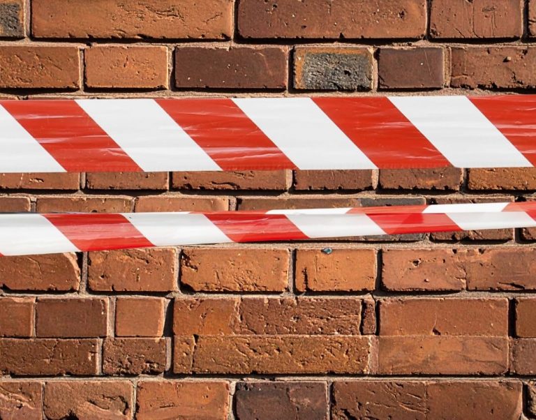 Rood-wit afzetlint gespannen voor een bakstenen muur, als waarschuwing of om een gebied af te sluiten.