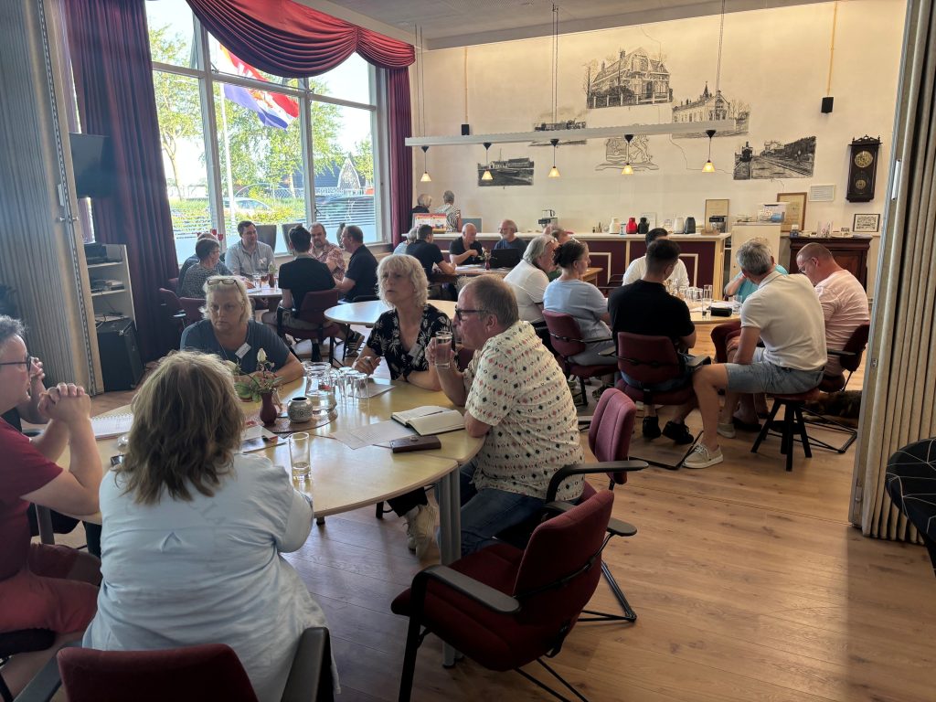 Mensen zitten bij elkaar aan tafeltjes tijdens het raadscafe