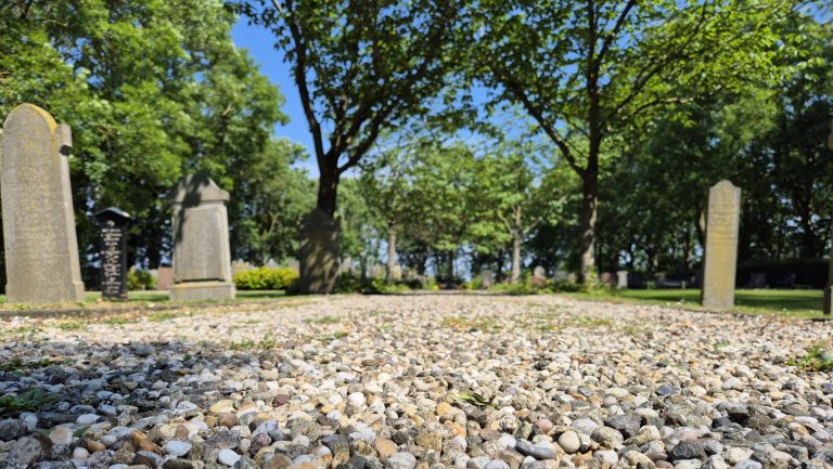 Werkzaamheden paden begraafplaatsen. Vanaf de grond genomen foto van een pad en enkele graven.