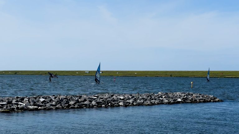 Lutjestrand aan het Amstelmeer met wind- en wingsurfers op het water en een stenen golfbreker op de voorgrond.